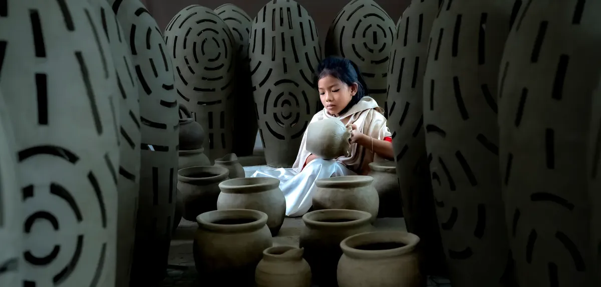 Young girl immersed in creating pottery surrounded by clay pots, showcasing cultural art.