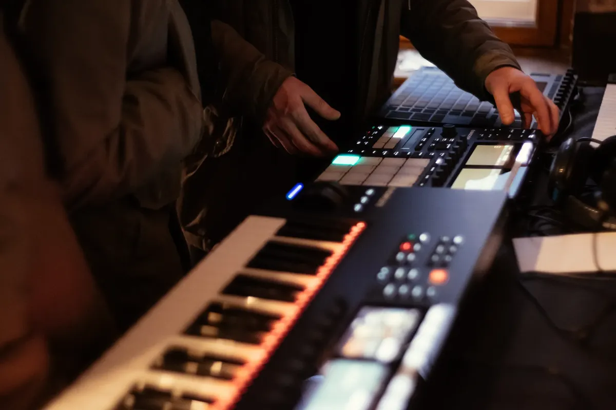 Music producer using synthesizer and beat pad in studio setting.